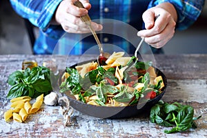 Chef mixes pasta with basil and spices in a pan. Appetizing pasta in a pan with tomatoes, basil and spices. One pan pasta. Italian