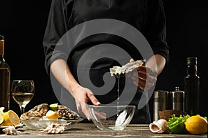 The chef opens and cleans the raw oyster against a background of white wine, lettuce, lemons and limes
