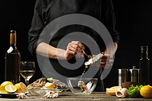 The chef opens and cleans the raw oyster against a background of white wine, lettuce, lemons and limes