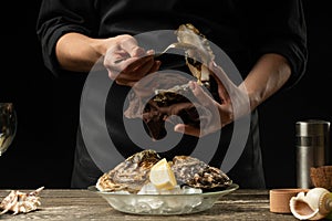 The chef opens and cleans the raw oyster against a background of white wine, lettuce, lemons and limes