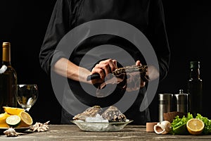 The chef opens the knife and cleans the raw oyster, on the background of white wine, lettuce, lemons and limes