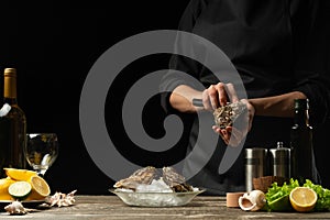 The chef opens the knife and cleans the raw oyster, on the background of white wine, lettuce, lemons and limes