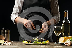 Chef opens a knife with mussels with a salad with white wine, on a dark background, the concept of the restaurant, menu and hotel