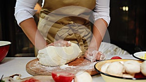 Chef pastry hands, kneading a yeast dough with scattered flour on wooden cutting board in a rustic kitchen. Baking bread