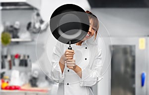 chef peeking out from behind frying pan on kitchen