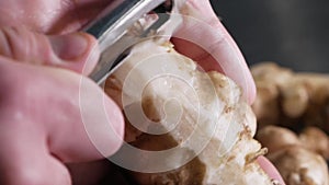 Chef peeling raw fresh jerusalem artichokes or ginger close up.