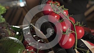 Chef picking bunch of tomatoes from a basket of herbs with a gloved hand