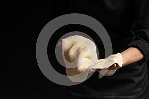 Chef pizza maker preparing pizza, holding rolled dough in hands. On a black background for design