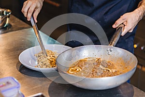 Chef plating cooked Wagyu Ragu with Tagliatelle pasta in white plate