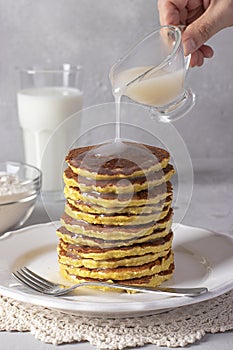 Chef pouring condensed coconut milk on coconut flour pancakes, vegan food, gray background