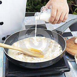 Chef pouring fresh milk the pan for cooking mushroom cream soup