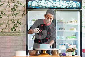 Asian male pastry chef wearing black uniform pouring melted chocolated to round blue cake photo