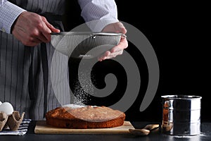 Chef pouring powdered sugar on tasty pie on dark background. ched processing pie or cake