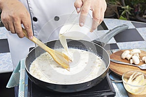 Chef pouring whipping cream in the pan for cooking mushroom cream soup