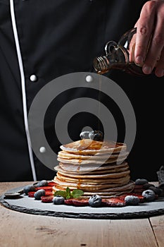 The chef pours maple syrup on pancake stack with blueberries and