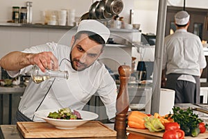 Chef pours olive oil into bowl of salad on kitchen. Cooking tasty and healthy food