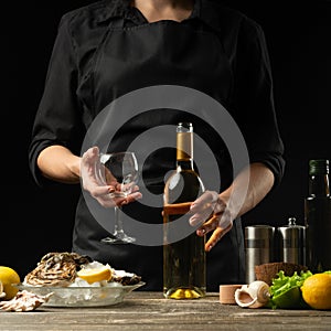 Chef pours, tastes Italian dry wine with oysters with lemon on a black background, the concept of seafood, wine, menus, recipes,