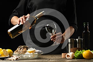 Chef pours, tastes Italian dry wine with oysters with lemon on a black background, the concept of seafood, wine, menus, recipes,