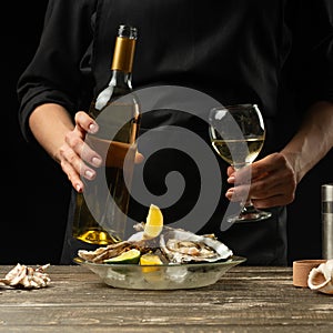 Chef pours, tastes Italian dry wine with oysters with lemon on a black background, the concept of seafood, wine, menus, recipes,