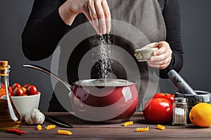 The chef preparations spaghetti and pasta, salt water, against a dark background, the concept of cooking. Woman salting water