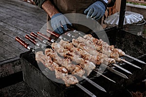 The chef prepares chicken shish kebab. Street food. Meat cooked over a fire, BBQ party in the backyard. Male hands in gloves hold