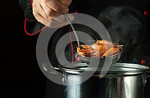 The chef prepares delicious shrimp in a pot in the restaurant kitchen. Cooking seafood, healthy vegetarian food and meal on dark