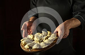 The chef prepares dumplings in the kitchen. Cutting board with raw dumplings in the cook hand. Copy space