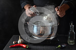 The chef prepares dumplings in a saucepan in the restaurant kitchen. Close-up hands of the cook add salt. Free ad space