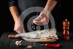 The chef prepares fresh fish sprinkling salt. Preparing to cook fish food. Working environment in the restaurant kitchen