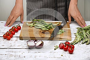 The chef prepares green beans, tomatoes on a branch, red onions in the white kitchen.