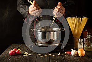 Chef prepares Italian pasta in a saucepan with vegetables. Close-up of cook hands while cooking in kitchen. Cucina italiana photo