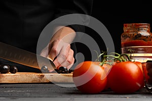 Chef prepares pizza, slices olives, on the background with ingredients. Recipe book, menu, home cooking, pizzeria