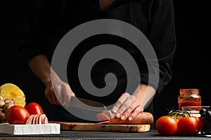 Chef prepares pizza, slicing fresh salami, on the background with ingredients. Recipe book, menu, home cooking