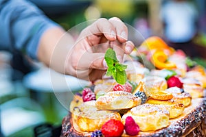 Chef prepares a plate of cakes with fresh fruits. He is working on the herb decoration. Outdoor garden party