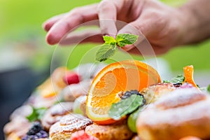 Chef prepares a plate of cakes with fresh fruits. He is working on the herb decoration. Outdoor garden party