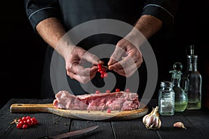 The chef prepares raw veal meat. Before baking, the cook puts the viburnum on the beef. National dish is being prepared in the