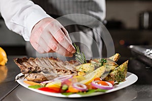 The chef prepares in the restaurant. Grilled rack of lamb with fried potatoes and fresh vegetables. closeup