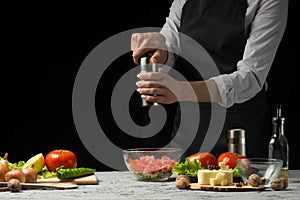 The chef prepares a salad, with a Pepper mill on a dark background with an empty space for writing