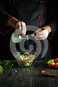 A chef prepares a vegetable salad in a restaurant kitchen. Add apple cider vinegar to cucumber and tomato salad. Place for recipe