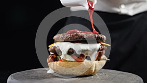 Chef preparing juicy burger and pours spicy sauce on it making burgers at fast food restaurant, Slow motion. Chef