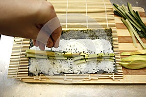 Chef preparing maki sushi by rolling nori seaweed,rice and fish on makisu bamboo mat.