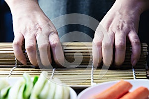 Chef preparing sushi roll over black table background