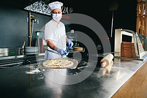 Chef  with protective coronavirus face mask preparing pizza