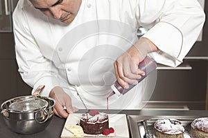 Chef Puts Finishing Touches On Chocolate Cake At Kitchen Counter photo