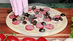 The chef puts sliced black olives on top of the raw pizza as he prepares to bake it.