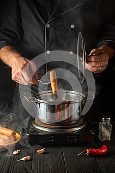 Chef puts Vienna sausage in a saucepan. Working environment in the kitchen of a restaurant or cafe. Preparing breakfast or lunch