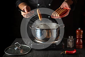 Chef puts Vienna sausage in a saucepan. Working environment in the kitchen of a restaurant or cafe. Preparing breakfast or lunch