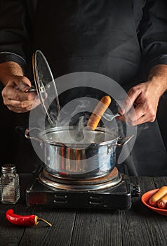 Chef puts Vienna sausage in a saucepan. Working environment in the kitchen of a restaurant or cafe. Preparing breakfast or lunch