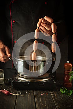 The chef puts the Viennese sausages into the pan. Working environment in the kitchen of a restaurant or cafe. Preparing breakfast