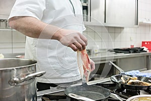 Chef putting ham into frying pan on stove in restaurant kitchen